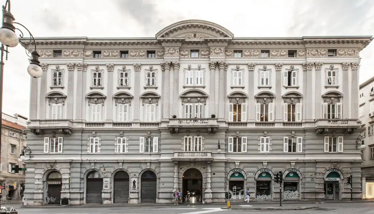 Facciata neoclassica grigia di Palazzo Diana, sede di R/STARS, con balconi, finestre bianche e negozi Tigotà ad archi